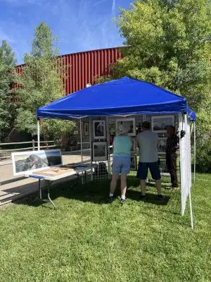 People look at artworks set up in pop-up tent outside.