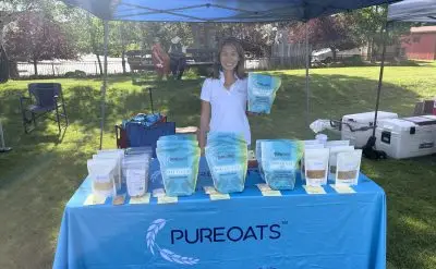 A smiling woman holds up a package at a farmer's market stand.