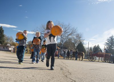 Kids walk across a parking lot holding pumpkins.