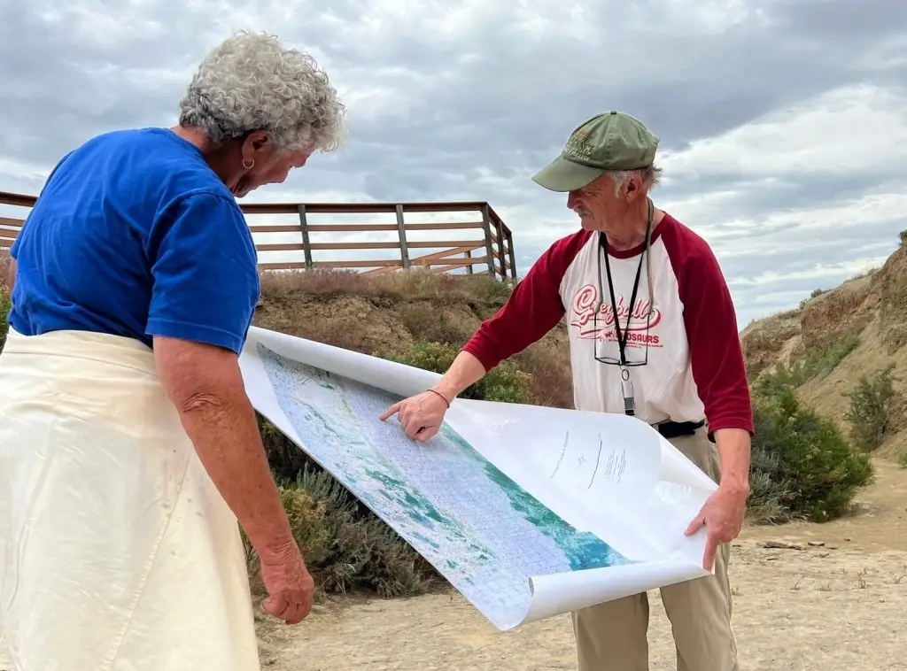 woman looks on as man wearing Greybull Dinosaurs T-shirt points to a location on a large map