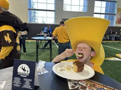 A young boy in a huge yellow hat eating cake