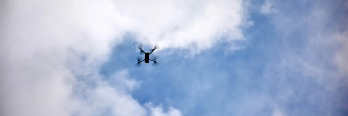 Drone flies across a blue sky mixed with clouds