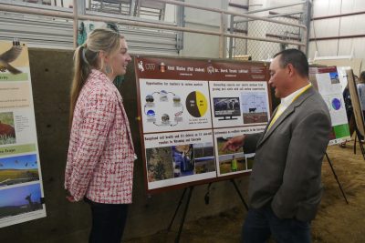 A young woman stands next to a scientific poster while a man looks at the poster.