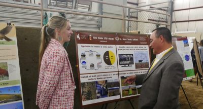 A young woman stands next to a scientific poster while a man looks at the poster.