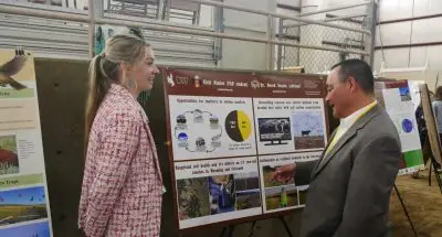 A young woman stands next to a scientific poster while a man looks at the poster.