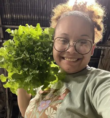 Selfie of a smiling woman holding up a large head of leafy green lettuce