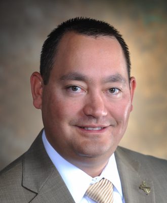 Portrait of smiling man wearing formal attire with small gold Wyoming pin on his lapel