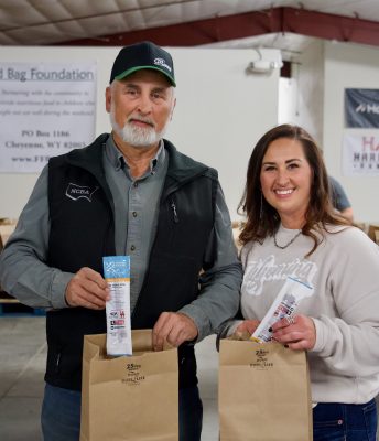 A man and woman placing beef jerky sticks in paper bags.