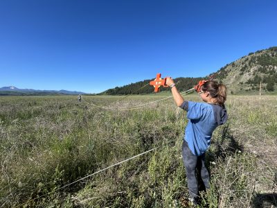 A young woman holding up two tape measures in a grassy field.