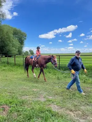 A young girl rides a brown horse with a man walking in front leading the horse.