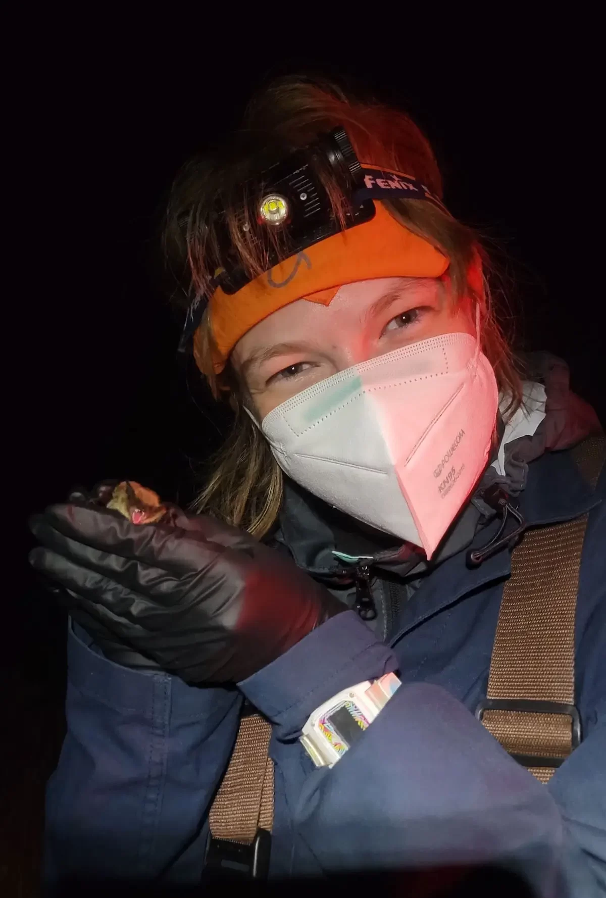 Renee Lile woman wearing a headlamp, gloves, a mask, and warm clothing holding a bat.