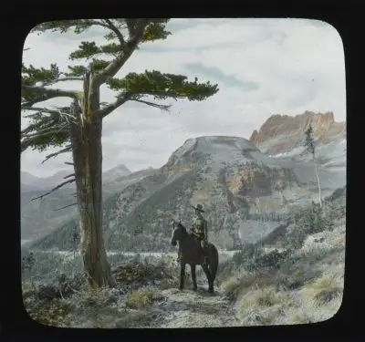 A photo of a man on a horse on a mountain trail. The image's colors are somewhat muted; it appears like it was taken with an old camera.