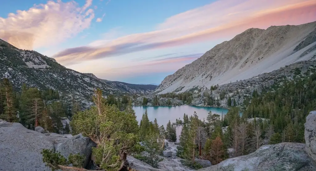 Colorful sunset over a turquoise alpine lake surrounded by rocky slopes and pine trees