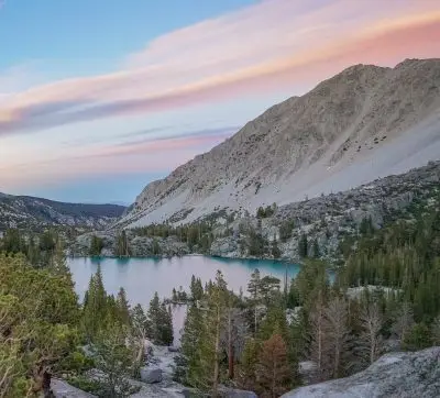 Colorful sunset over a turquoise alpine lake surrounded by rocky slopes and pine trees