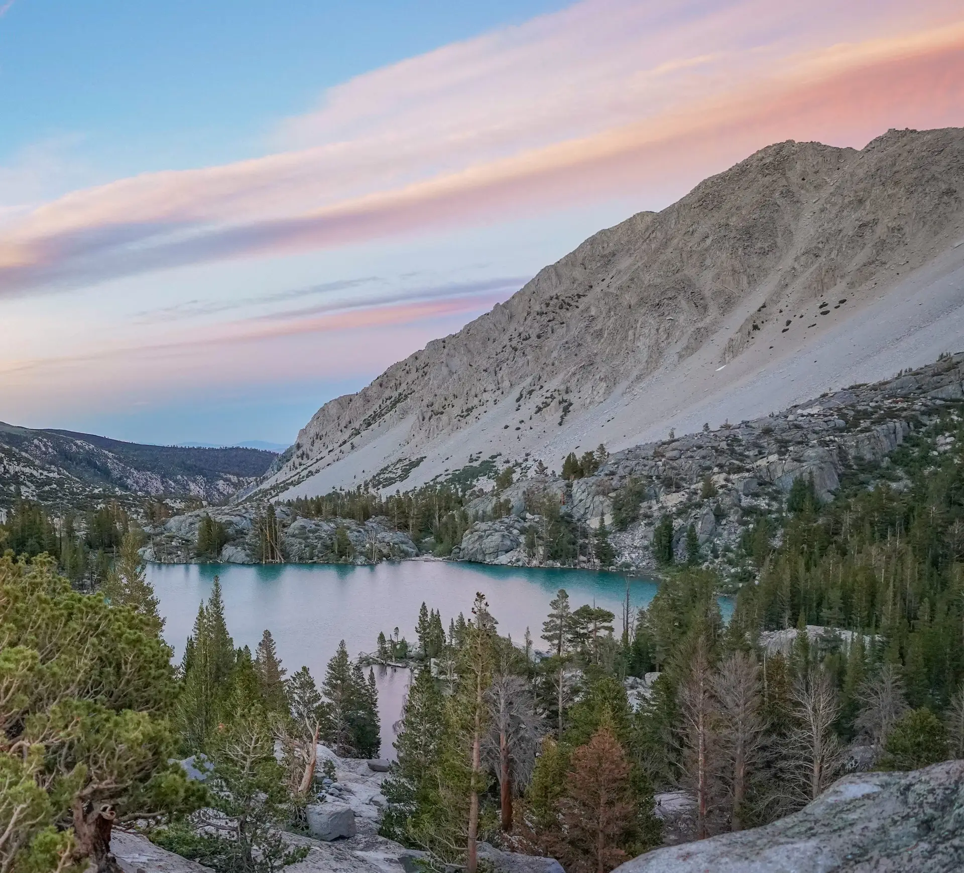 Colorful sunset over a turquoise alpine lake surrounded by rocky slopes and pine trees