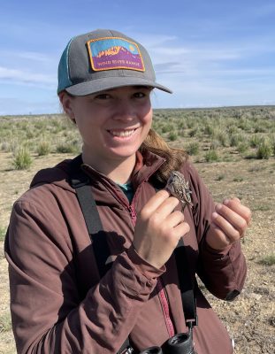 A woman in a field holding a very small bird.