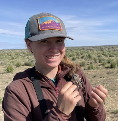 A woman in a field holding a very small bird.