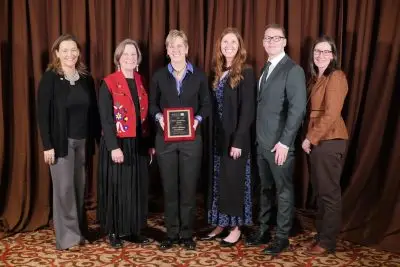A group of people in fancy clothing. The person in the middle is holding a plaque.