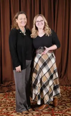 Two women in formal clothing. The woman on the right is holding a small glass plaque.