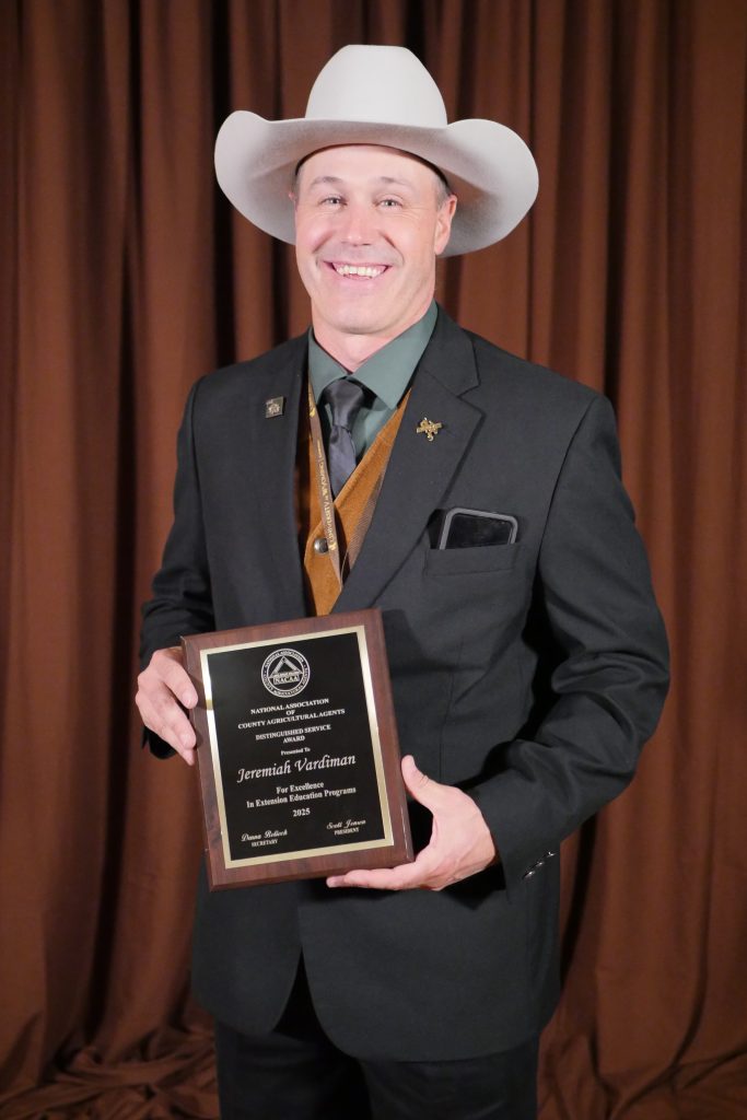 A man in formal clothing and a cowboy hat holding a plaque.
