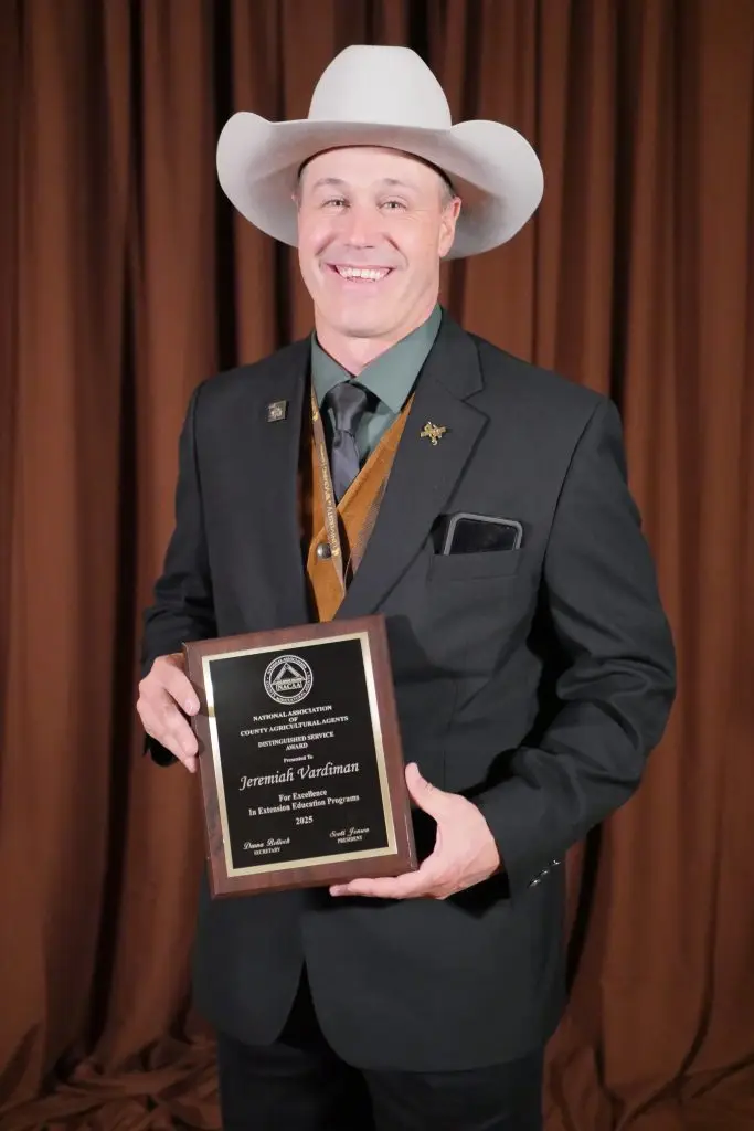 A man in formal clothing and a cowboy hat holding a plaque.