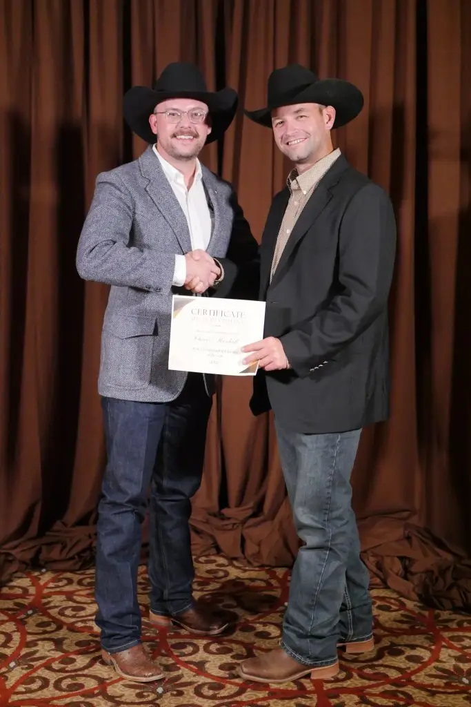 Two people in suit jackets, cowboy hats, and jeans.