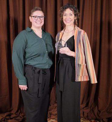 Two women in formal clothing. The woman on the right is holding a small glass plaque.