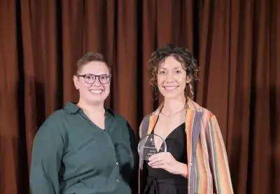 Two women in formal clothing. The woman on the right is holding a small glass plaque.