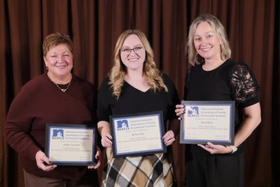 Three women in formal clothing holding plaques.