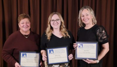 Three women in formal clothing holding plaques.