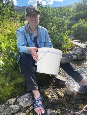 Anna Krepel holds a bucket while sitting on the edge of a stream. 
