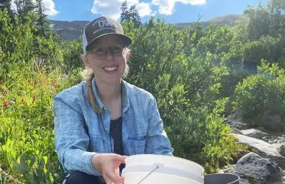 Anna Krepel holds a bucket while sitting on the edge of a stream.