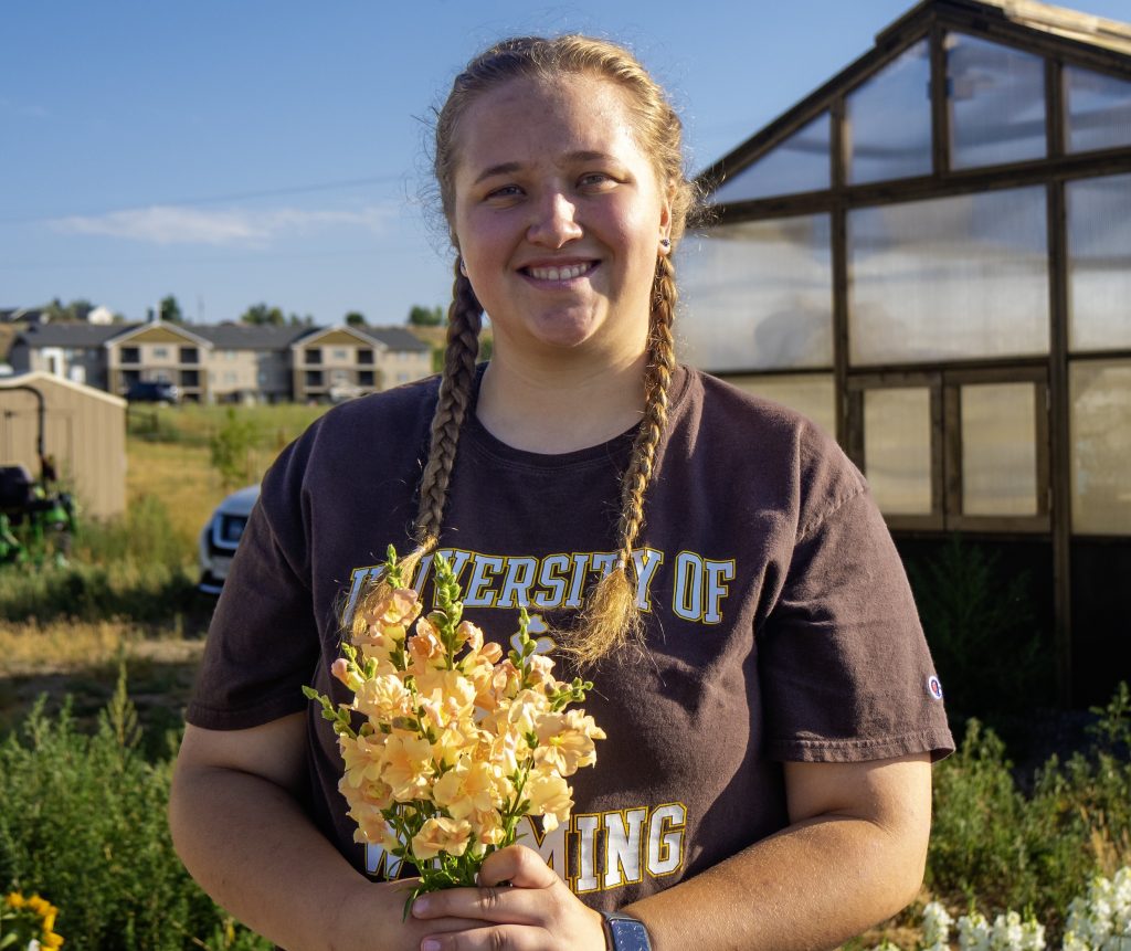 Courtney standing in front of a greenhouse wearing a UW shirt and holding a bunch of snapdragons
