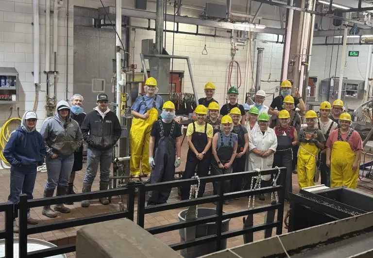 group of people, most wearing hard hats, boots, and protective coveralls, in an indoor space equipped with meat processing equipment