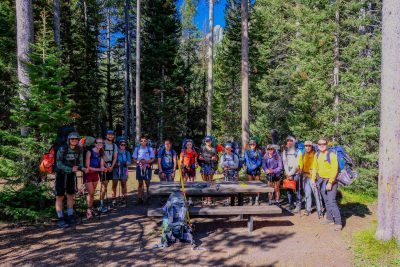 A group of people poses in a campsite surrounded by trees.