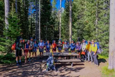 A group of people poses in a campsite surrounded by trees.