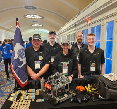 four teens and their coach stand behind a table with their robot and a Wyoming state flag