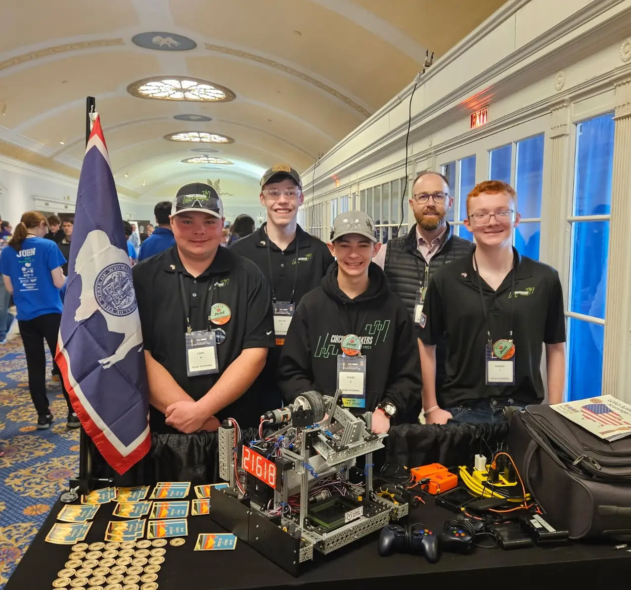 four teens and their coach stand behind a table with their robot and a Wyoming state flag