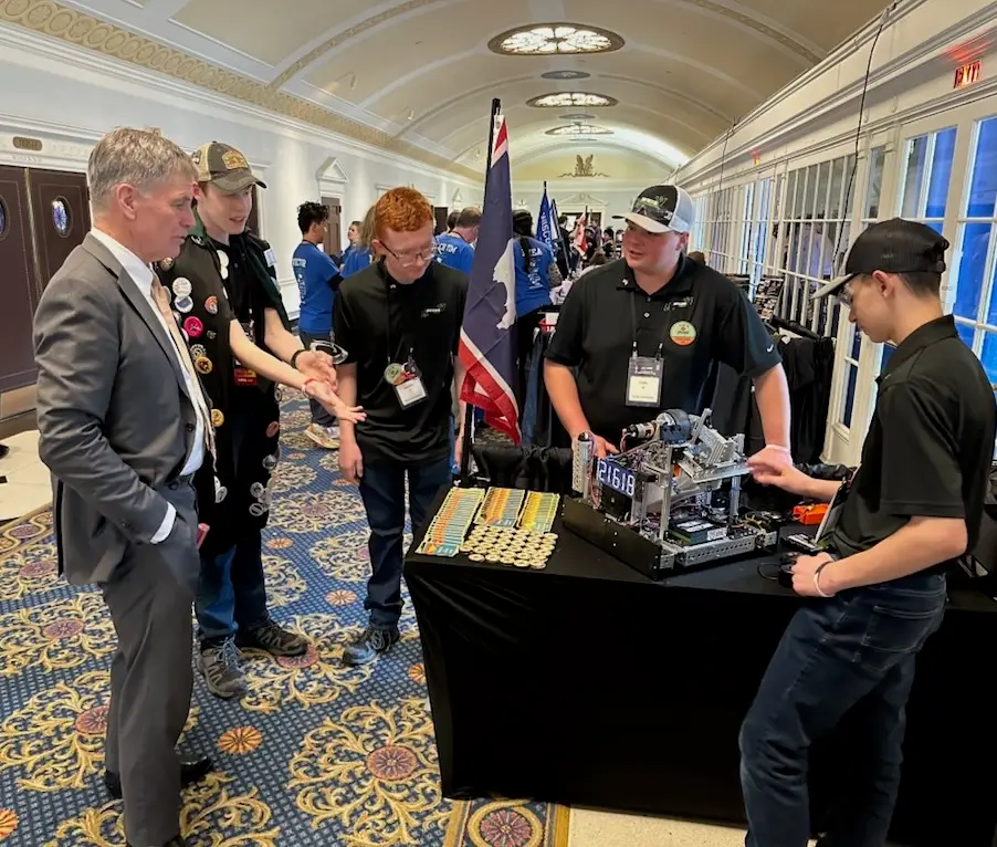 The Circuit Breakers gather around a table with their robot and a Wyoming flag while chatting with Governor Gordon