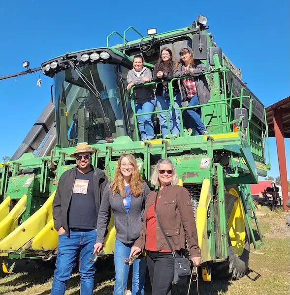 Six people in front of a large tractor.