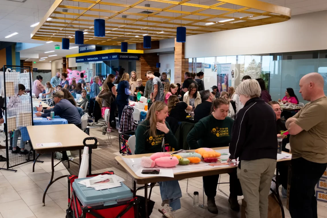 Crowd of youth and families gathered indoors, visiting activity booths and interacting with exhibitors at a community event.