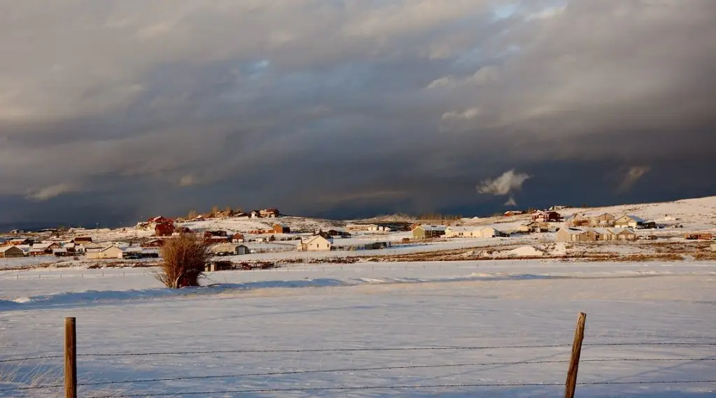 A snowy, rural landscape with some open space and some houses.