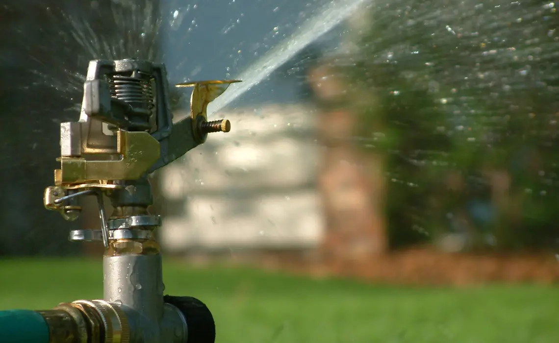 Close-up of a lawn sprinkler spraying water across a grassy yard