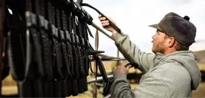 A ranch manager wearing a gray hoodie and dark cap hangs electronic livestock collars on a rack at Pitchfork Ranch in Park County as part of the ranch’s virtual fencing system.