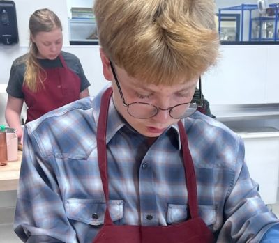 boy wearing apron and glasses forms a homemade tortilla on a wooden-topped counter