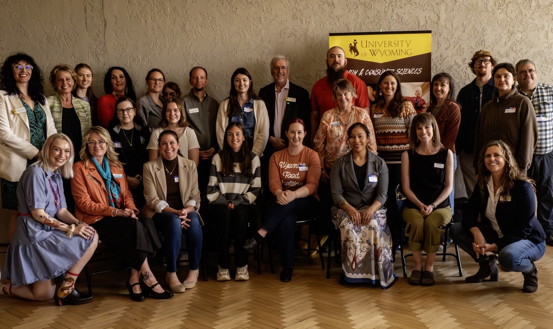 large group of people organized into two rows pose together next to a sign advertising UW's Department of Family and Consumer Sciences
