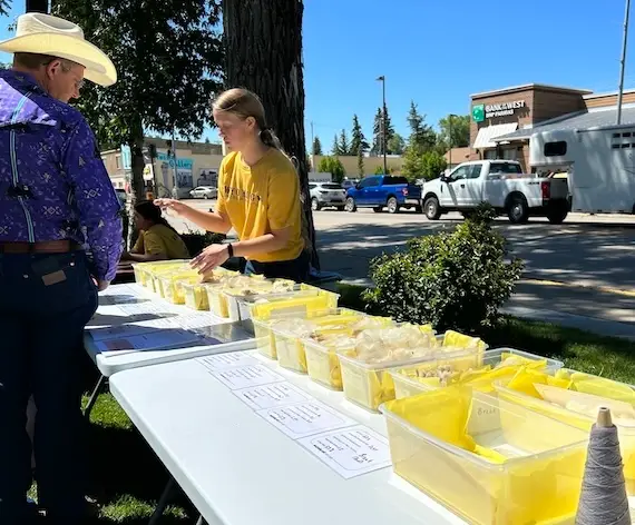 student standing behind a table gestures toward a line of wool samples while chatting with an event participant