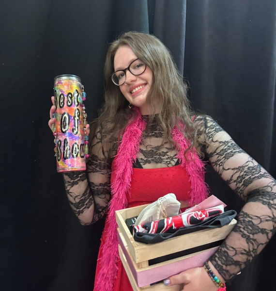 Izzy Nichols smiles while holding a colorful tumbler and a box of fashion items after winning awards at the 2026 Kaleidoscope Fashion Show.