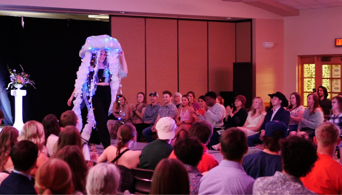 Model wearing an illuminated jellyfish-inspired outfit walks the runway as audience members applaud at UW’s 2023 Kaleidoscope Fashion Show.