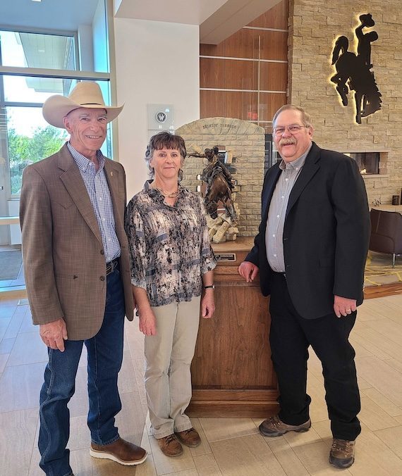 Doug Stark, Deniz Stark, and Chris Bastian stand in front of a statue of a horse rider breaking through a wall.